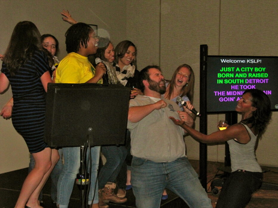 karaoke singers on stage around guy on his knees singing "Don't stop Believing"by Journey
